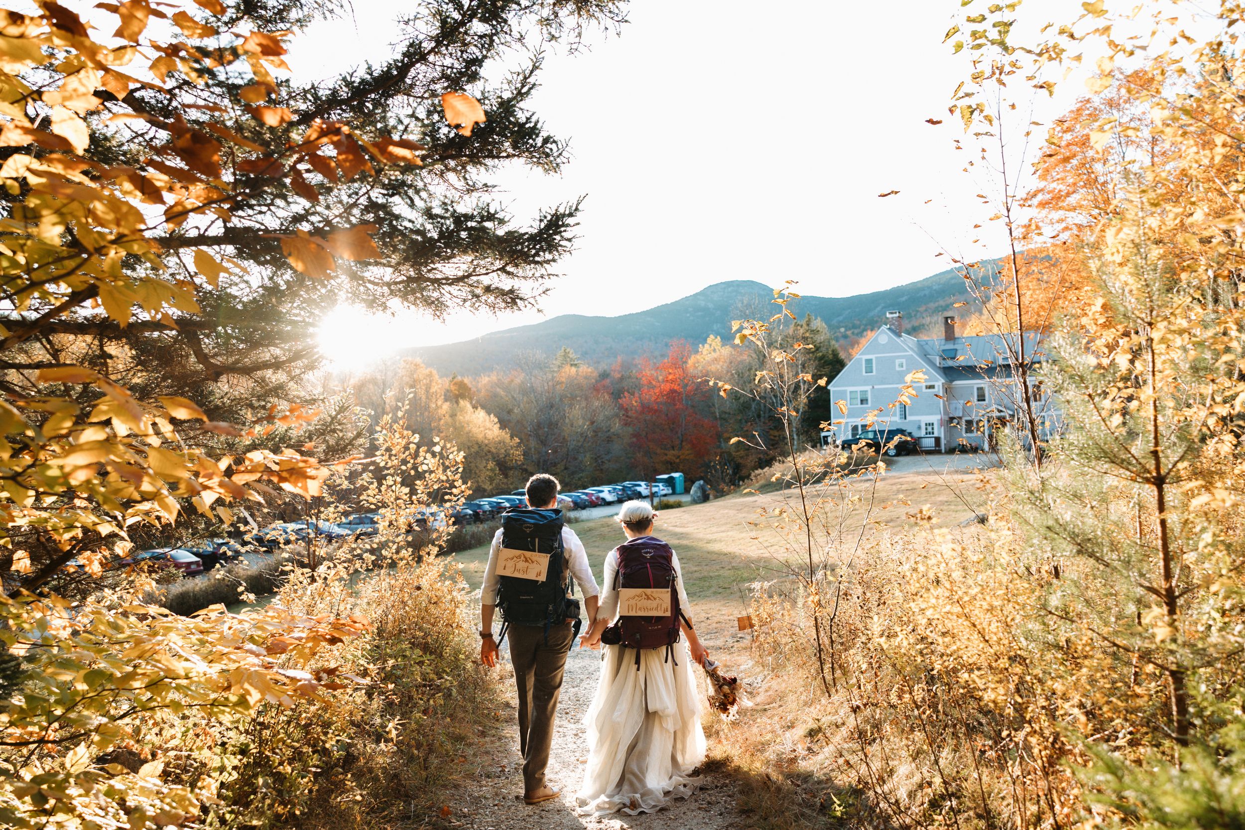 Bride and groom walking hand in hand on a wooded trail at AMC Cardigan Lodge in New Hampshire during a fall mountain wedding.