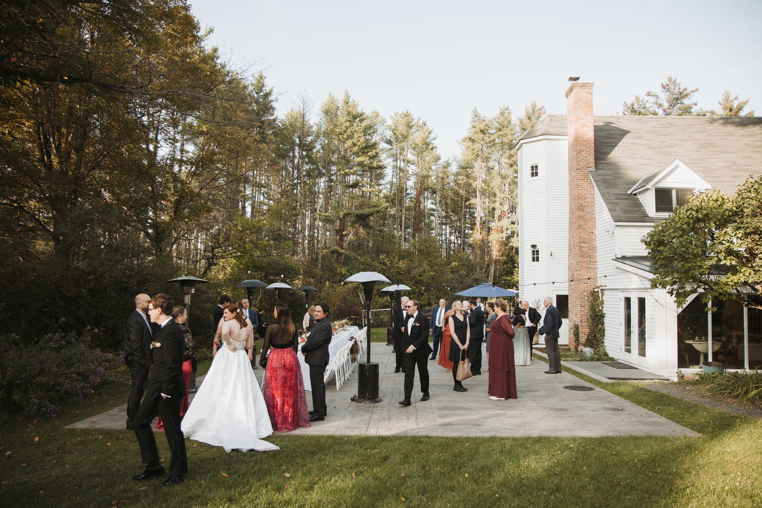 Outdoor wedding cocktail hour at The Inn at Weathersfield in Vermont with guests gathered on the lawn beside the white inn building surrounded by trees.